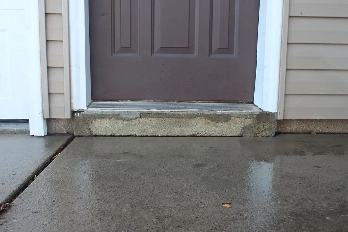 A wet cement floor with a door and door frame, showcasing a damp surface and lifted concrete.