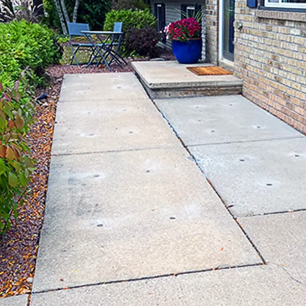 A sidewalk adorned with a flower pot and chairs, showing drill holes.